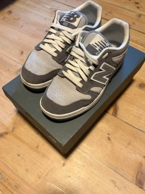 New Balance 480 gråvita sneakers - Snygga New Balance 480 sneakers i grått och vitt med klassisk N-logga på sidan. Ovandelen är i mocka och mesh för en skön och luftig känsla. Lågt skaft och vita snören ger en clean look som passar till det mesta. Perfekta för dig som gillar stilrena och bekväma sneakers.