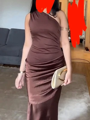 Brun one shoulder långklänning - Snygg brun långklänning i glansigt material med one shoulder-design. Klänningen har en åtsittande passform och fina draperingar längs midjan och höften. Perfekt för dig som vill sticka ut med en elegant och modern look. Köpt i Istanbul, använd 1 gång och är som ny. Storlek S