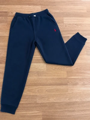 Ralph Lauren byxor - Säljer ett par stilrena mörkblå mjukisbyxor från Ralph Lauren med broderad röd logga. Superbekväma och perfekta både till vardags och för en avslappnad look. Byxorna har resår och dragsko i midjan samt fickor på sidorna. Självklart äkta!✅ • Färg: mörkblå • Broderad Ralph Lauren-logga • Resår i midja och benslut • Sidofickor • Skick: mycket fint skick men den är lite nopprig!
