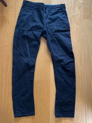 Svarta chinos med smal passform - Snygga svarta chinos med smal passform och klassisk design. Byxorna har två sidofickor och två bakfickor. Tillverkade i ett mjukt och bekvämt bomullsmaterial som passar perfekt till en avslappnad stil.