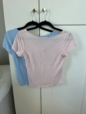 Två croppade toppar i pastell - Säljer två croppade toppar i pastellfärger, en ljusrosa och en ljusblå. Båda har korta ärmar och rundad halsringning. Perfekta att matcha med jeans eller kjol för en enkel och fräsch look.