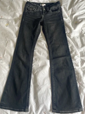 Svarta bootcut jeans från Gina Tricot - Säljer ett par svarta bootcut jeans från Gina Tricot med kontrastsömmar i vitt. Jeansen har klassisk femficksmodell, normal midja och är tillverkade i denim. Perfekta för dig som gillar en retro vibe och vill ha något som sticker ut.