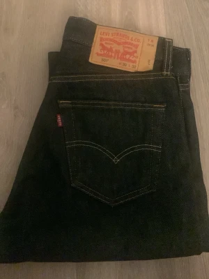 Levi's 501 charcoal svart shrink to fit - Klassiska Levi's 501 jeans i mörkblå denim med raka ben och femficksmodell. Tydliga kontrastsömmar och den ikoniska röda Levi's-lappen på bakfickan. Tillverkade i slitstarkt bomullsmaterial och har läderpatch bak i midjan. Det står 30-32 det det känns som 28-32