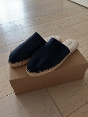 The Resort & Co- mocka mules  - Snygga Navy slip-in tofflor med ovandel i velour material och flätad sula i naturfärgad jute. Tofflorna har en stilren och enkel design med rundad tå och öppen häl. Helt nya. Kostar 134 euro nya säljer för 90€