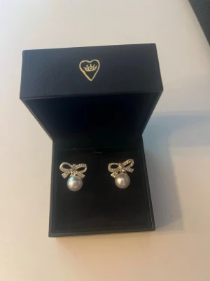  Silverörhängen med en rosett och pärlor - Ett par eleganta örhängen med gnistrande rosetter i silverfärg och vita pärlor. Rosetterna är dekorerade med små stenar som ger extra glans. Perfekt accessoar för att lyfta din stil.💗