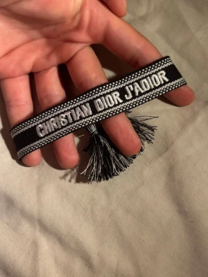 Christian Dior J'Adior svart armband - Snyggt svart och vitt tygarmband från Christian Dior med texten 'CHRISTIAN DIOR J'ADIOR' broderad. Helt ny, fraktas snabbt 