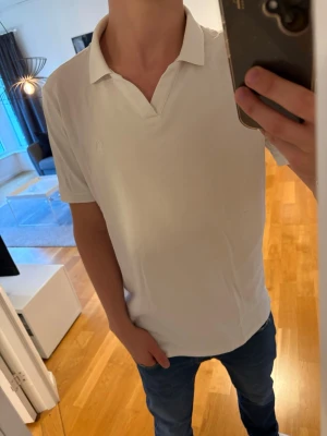 Vit pikétröja från Ralph Lauren - Klassisk vit pikétröja från Ralph Lauren med krage och korta ärmar. Tröjan har en diskret logga på bröstet och är tillverkad i mjuk bomull. Perfekt till jeans eller shorts för en clean och stilren look.