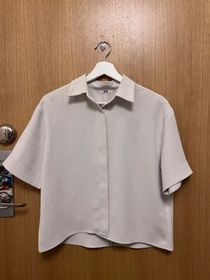 Vit kortärmad skjorta från Uniqlo - Stilren vit skjorta från Uniqlo i storlek XS. Skjortan har korta ärmar, klassisk krage och rak passform. Tillverkad i ett mjukt och lätt material som passar perfekt till alla tillfällen. Enkel och clean look som är lätt att matcha.