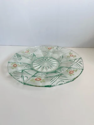 Glasfat med handmålat blommönster - Härligt serveringsfat / fruktfat / tallrik i glas med vackert handmålat blommönster i orange, gult och grönt. Transparent lätt grönt glas, pressat i ett detaljrikt geometriskt mönster. Diameter: 28 cm. Fint som serveringsfat eller som dekoration. Mycket gott skick!