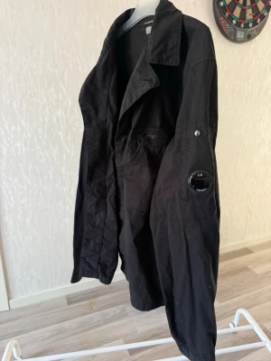Svart overshirt C.P. Company - Svart overshirt från C.P. Company med klassisk krage och ikonisk linsdetalj på ärmen. Väldigt bra till hösten samt våren aldrig för kall aldrig för varm. Nypris 3199kr