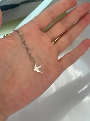 Silverfärgat halsband med fågelhänge - Snyggt halsband i silverfärg med ett stilrent fågelhänge. Kedjan är tunn och enkel, vilket gör att hänget verkligen står ut. Perfekt för dig som gillar minimalistiska smycken och vill ha något som känns unikt och personligt.