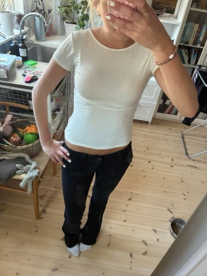 Vit topp med stor rosett i ryggen - Supersöt vit topp från lager 157 med tight passform och korta ärmar. Baksidan har en stor, iögonfallande rosett och öppen rygg som ger en unik look. Perfekt för dig som vill sticka ut lite extra! Materialet känns mjukt och stretchigt.