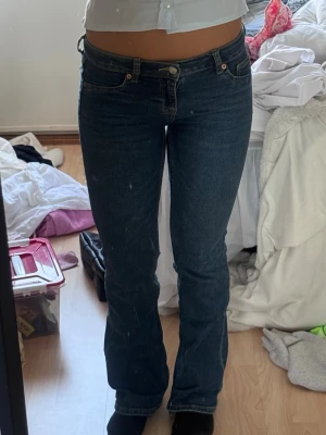 Mörkblå bootcut jeans - Säljer ett par mörkblå bootcut jeans med klassisk femficksdesign och normalhög midja. Jeansen har en snygg passform som sitter tight upptill och släpper ut vid bensluten. Tillverkade i stretchigt denimtyg för extra komfort.
