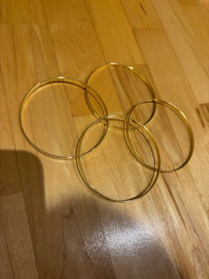 Tunna guldfärgade bangles armband - Säljer ett set med fyra tunna, runda bangles i guldfärgad metall. Armbanden har en enkel och stilren design som passar perfekt för att stapla flera tillsammans eller bära enskilt för en clean look.