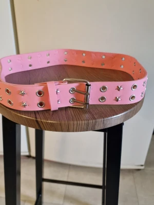 Skärp nitar rosa - Skärp nitar rosa. Nitbälte för kvinnor. Justerbart brett rosa bälte med metallspänne. 109 cm. Bredd 3,8 cm.