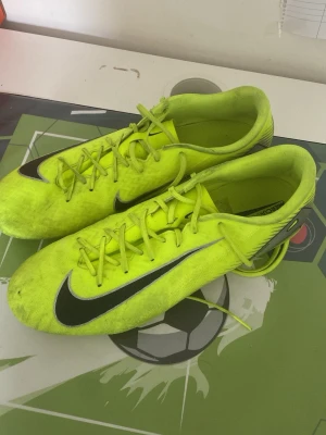 Neongula Nike fotbollsskor - Säljer ett par neongula Nike fotbollsskor med svart swoosh på sidan och snörning framtill. Skorna har en låg profil och är designade för bra grepp på planen. Perfekta för dig som vill sticka ut på matchen! Skorna är i pro nivå en nivå under elites och har bara testat en gång på planen men kände att de va lite för stora. Skorna kostade mig 1099 men säljer de halva priset.