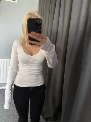 Vit långärmad topp från 157 - Säljer en vit långärmad topp från 157 med v-ringning och lätt rynkdetalj framtill. Toppen är i stretchigt material av bomull och elastan, sitter tight och har en clean look som passar till allt. Storleken var M men är insydd vid midjan så passar mer än S