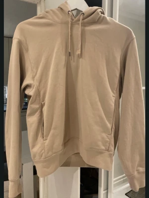Beige hoodie med huva och fickor - Snygg beige hoodie med huva och dragsko, perfekt för en avslappnad stil. Hoodien har en klassisk passform, långa ärmar och praktiska fickor på sidorna. Tillverkad i mjukt material som känns skönt mot huden.