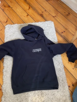Mörkblå hoodie med tryck Cactique - Snygg mörkblå hoodie med huva och stor magficka. På bröstet står det 'The Succulent Market of New York City CACTIQUE' i vitt tryck. Perfekt för dig som gillar streetwear och vill ha en chill look. Mjuk insida och klassisk passform. Ord pris 599