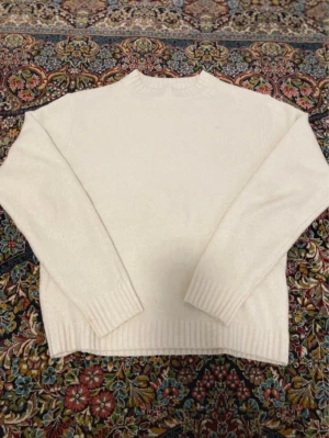 Vit stickad tröja från Uniqlo - Klassisk vit stickad tröja från Uniqlo i enkel design. Tröjan har rund hals, långa ärmar och ribbade muddar vid ärmslut och nederkant. Perfekt basplagg i mjukt material som passar till allt. (XS me passar som S)