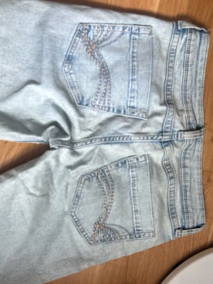 Lowwaist Ljusblå bootcut jeans med broderi - Säljer ett par ljusblå jeans med bootcut-modell och snygga broderade detaljer på bakfickorna. Jeansen har klassisk femficksdesign och är gjorda i denim. Perfekta för dig som gillar retrovibbar och vill ha ett par unika jeans i garderoben.