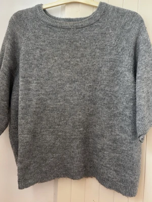 Grå oversized stickad tröja - Mysig grå stickad tröja i oversized modell med rund halsringning och långa ärmar. Tröjan har en enkel och stilren design, perfekt för lager på lager och chill dagar. Materialet ser ut att vara mjukt och lite luddigt, troligen ull- eller ullmix.