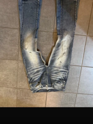 Blå slitna jeans från Purple Brand - Säljer ett par blå jeans från Purple Brand med snyggt slitna detaljer och ljusa partier på låren och knäna. Klassisk femficksmodell med gylf och knapp. Jeansen har en smal passform och cool tvätt som ger en trendig streetkänsla.