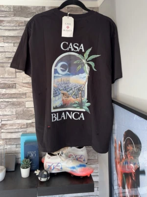 Svart Casablanca t-shirt med tryck - Säljer en svart t-shirt från Casablanca med färgglatt tryck av palmer och stadsmotiv både fram och bak. T-shirten har rund hals och korta ärmar. Perfekt för dig som gillar streetwear och vill sticka ut med en unik design. M men passar S modellen är 170cm typ 