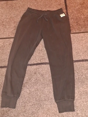 Svarta mjukisbyxor med dragsko size L  - Svarta mjukisbyxor med resår i midjan och dragsko för skön passform. Byxorna har ribbade muddar vid bensluten och en enkel, stilren design. Perfekta för chill eller träning. Size L 
