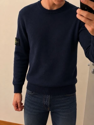 Stone Island Mörkblå Tröja - Mörkblå rundhalsad tröja från Stone Island med klassisk patch på vänster ärm. Tröjan har ribbade muddar vid ärmslut och nederkant, och är tillverkad i mjukt material som passar perfekt till jeans. Tröjan är dock lite solblekt på vissa ställen, därför det låga priset. Är egentligen typ L/XL men sitter mer som en M.