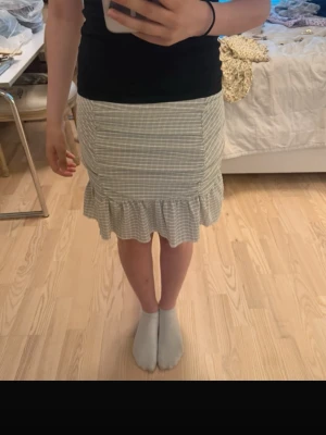 Beige rutig volangkjol Gina Tricot - Supersöt beige och vit rutig kjol från Gina Tricot i storlek S. Kjolen har en figurnära passform och avslutas med en volangkant nedtill. Perfekt för dig som gillar en feminin och trendig stil. Tillverkad i mjuk bomullsmix.