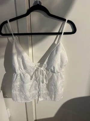 Vit broderad linnetopp med knyt - Söt vit linnetopp med tunna axelband och broderade blommor. Toppen har v-ringning och knyt framtill, samt är croppad i modellen. Perfekt att styla med båge jeans eller en kjol💕 har tyvärr tagit bort lappen så vet ej vart den är ifrån då jag fått den i present 🤧