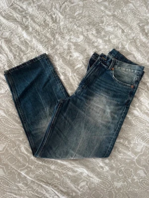 Weekday jeans - Säljer ett par klassiska blå jeans med raka ben och snygga slitningar framtill. Jeansen har fem fickor och kopparfärgade nitar.  Storlek 30/30. 