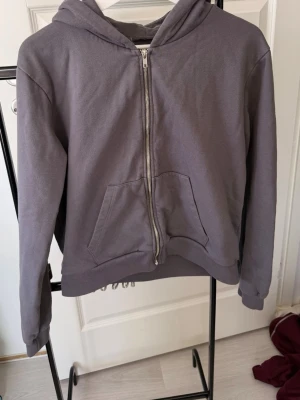 Grå zip hoodie med huva - En enkel grå hoodie med dragkedja framtill och stor ficka på magen. Hoodien har huva och ribbade muddar vid ärmar och nederkant. Perfekt för en avslappnad stil och passar till det mesta. Materialet känns mjukt och bekvämt.