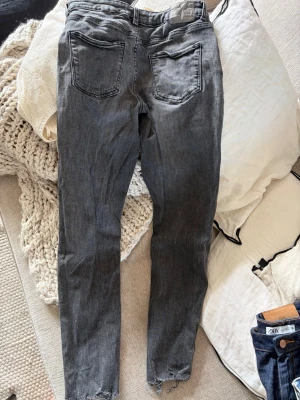 Grå jeans från ZARA med rå kant - Säljer ett par grå jeans från ZARA i storlek 38. Jeansen har raka ben, två bakfickor och en snygg rå kant nedtill. Tillverkade i klassisk denim med en tvättad look som ger en avslappnad vibe.