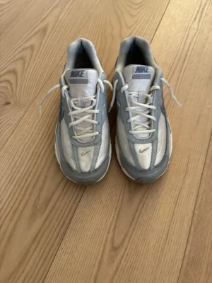 Nike vita och grå sneakers - Nike sneakers i vitt och ljusgrått med mesh och syntetpaneler. Klassisk låg modell med vit sula och grå detaljer, samt Nike-logga på sidan och plösen. Skorna har vita snören och en sportig, retroinspirerad design. Säljer dom eftersom att dom inte passar längre!