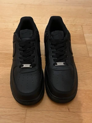 Nike Air Force 1  - Säljer ett par helt oanvända helsvarta Nike Air Force 1 i storlek 40 då de är för små. Skorna har svart svart sula och svarta skosnören. Men även en metallbricka med 'AF1' på snörningen som ger en extra detalj. Perfekta för dig som gillar stilrena sneakers. Hör gärna av dig om du skulle ha någon fråga.