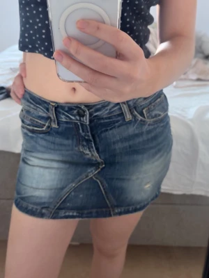 Blå jeanskjol från ONLY - Säljer en blå jeanskjol från ONLY med slitna detaljer och klassisk femficksdesign. Kjolen har en kort passform och markerade sömmar framtill som ger en cool look. Perfekt till sommaren och enkel att matcha med olika toppar.