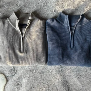 Två halvzip tröjor i beige och blå - Säljer två stilrena halvzip tröjor i ribbstickad bomull, en i beige och en i blått. Perfekta för lager på lager och har hög krage med dragkedja. Passar dig som gillar en clean och avslappnad look. 1st/200kr, 2st/350kr