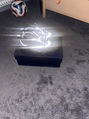 Dior b22 Svarta och vita sneakers med reflexdetaljer - Säljer ett par snygga sneakers i svart och vitt med tydliga reflexdetaljer som lyser upp i blixtljus. Skorna har meshpaneler för bra ventilation och grov sula för extra komfort. Perfekta för dig som vill sticka ut med coola detaljer och sportig look.