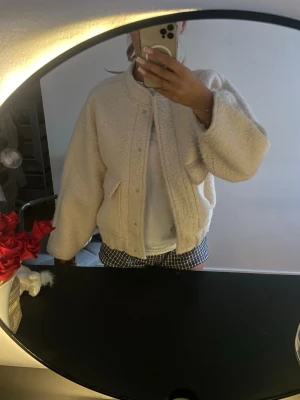 Beige teddyjacka med stora fickor - Säljer en beige teddyjacka med oversized passform och stora fickor framtill. Jackan har rund halsringning, dold dragkedja och tryckknappar. Materialet är fluffigt och mjukt, perfekt för att hålla värmen. Enkel och stilren design som passar till det mesta.