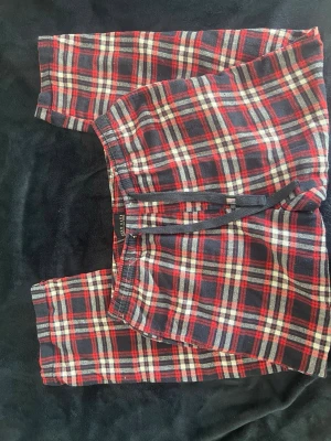 Rutiga pyjamasbyxor i flanell - Mysiga pyjamasbyxor i mjuk flanell med klassiskt rutigt mönster i rött, svart och vitt. Byxorna har resår i midjan och snörning för extra komfort. Perfekta för slappa dagar hemma eller sköna nätter.