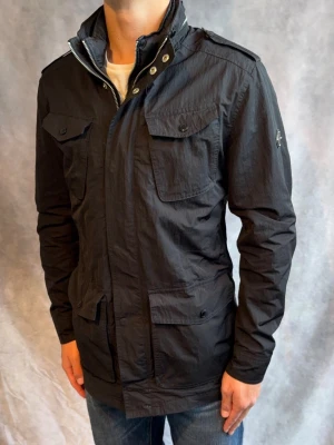 J-Lindberg Fieldjacket - Stl M - Riktigt snygg Höst/vinterjacka från J-Lindeberg i färgen svart! | Mycket bra skick: 8/10, små fläckar på bröstet syns inte väll från längre avstånd | Stl: M, modellen är 178cm och väger 78kg, passar bra mellan 178-188cm 🙌  | Hör av dig vid frågor // Galgen 🫡 Har fler Jackor i profilen samt om du köper mer plagg blir de billigare!