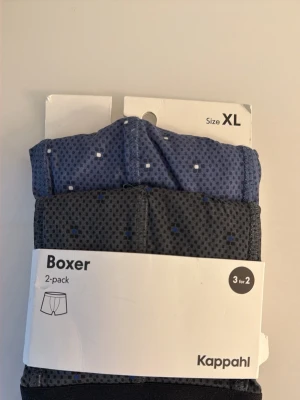 2-pack boxerkalsonger Kappahl XL - Säljer ett 2-pack boxerkalsonger från Kappahl i storlek XL. Ena paret är blått och det andra är mörkgrått, båda med små fyrkantiga mönster i vitt och blått. Bred resår i midjan för skön passform. Perfekta för dig som vill ha stilrena och bekväma kalsonger.