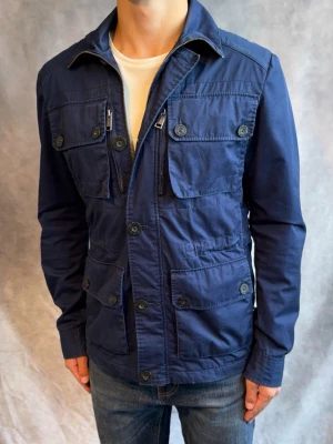 J-Lindeberg Fieldjacket marinblå - Stl M - Riktigt snygg Höst/vår Fieldjacket från J-Lindeberg i färgen marinblå! | Mycket bra skick: 9/10, mindre spår av användning | Stl: M dock så är Storlekslappen borta, modellen är 178cm och väger 78kg, passar bra mellan 177-188cm 🙌  | Hör av dig vid frågor // Galgen 🫡 Har fler Jackor i profilen samt om du köper mer plagg blir de billigare!