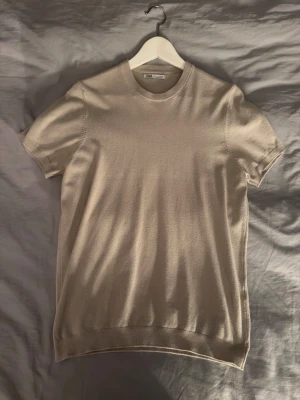 Beige kortärmad t-shirt i bomull - Snygg beige t-shirt med rund hals och korta ärmar. Tillverkad i mjuk bomull som känns skön mot huden. Enkel och stilren design utan tryck eller mönster, perfekt till alla typer av outfits.