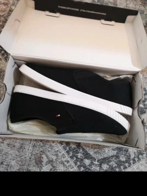 Svarta slip-on sneakers Tommy Hilfiger - Modellen är väldigt smal, passade inte mig som normalt är en 38, gissar på att den passar 37-37,5 eller en liten 38 med smala fötter Ej säker på om det är äkta