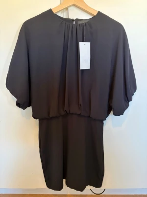 Svart kortklänning med vida ärmar - ZARA Black Dress – New with Tags 🖤  Elegant black dress from ZARA with a flattering draped design and relaxed sleeves. Perfect for parties, dinners or an elegant everyday look.  • Size: S • Color: Black • Condition: New with tags • Original price: 399 SEK • Article no.: 8372/039/800  Never worn ✨