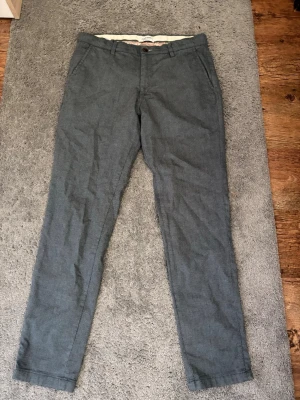 Blå chinos från Jack & Jones - Snygga blå chinos från Jack & Jones med diskret mönster i tyget. Klassisk rak passform med fickor fram och bak samt bälteshällor. Stängs med knapp och dragkedja. Perfekta för en stilren och avslappnad look.