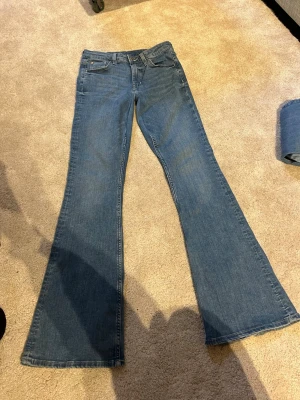 Blå bootcut jeans med låg midja - Säljer ett par klassiska blå bootcut jeans. Jeansen är från hm och är i storlek 38. De är omsydda till lågmidjade (inte märkbart när man har på sig jeansen). Och de har små slitningar i benen